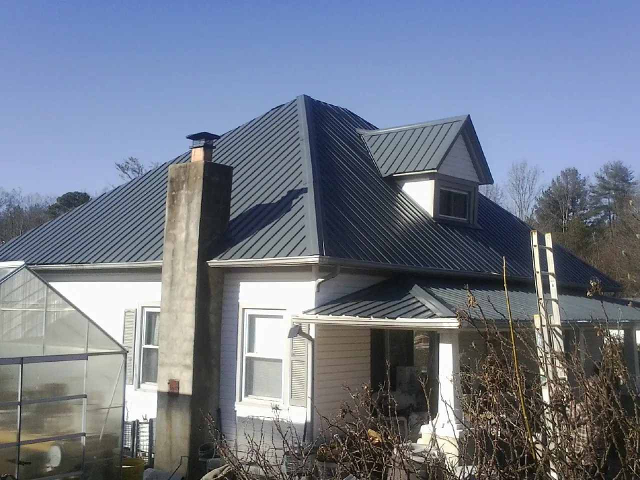 Dark blue standing seam metal roof on a white farmhouse with dormer — Slate & Tile Roof Repair by Roofing Brothers in Wichita