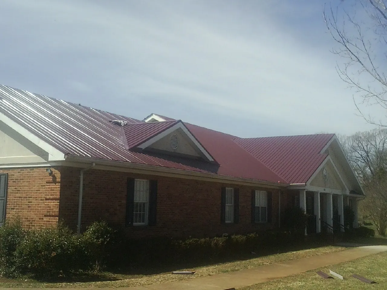 Red metal roof with gabled entries on a long brick building, from a Hail Damage Roof Repair job in Wichita