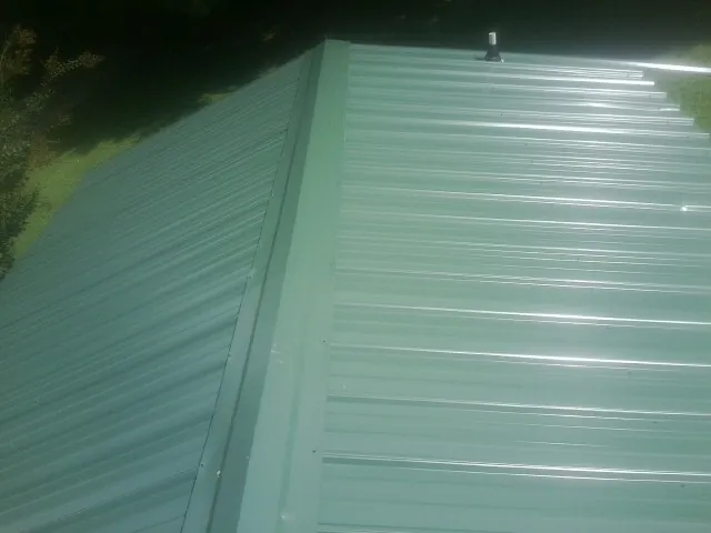 New green metal panels meeting at the ridge of a roof — Flat Roof Repair work by our crew in Wichita
