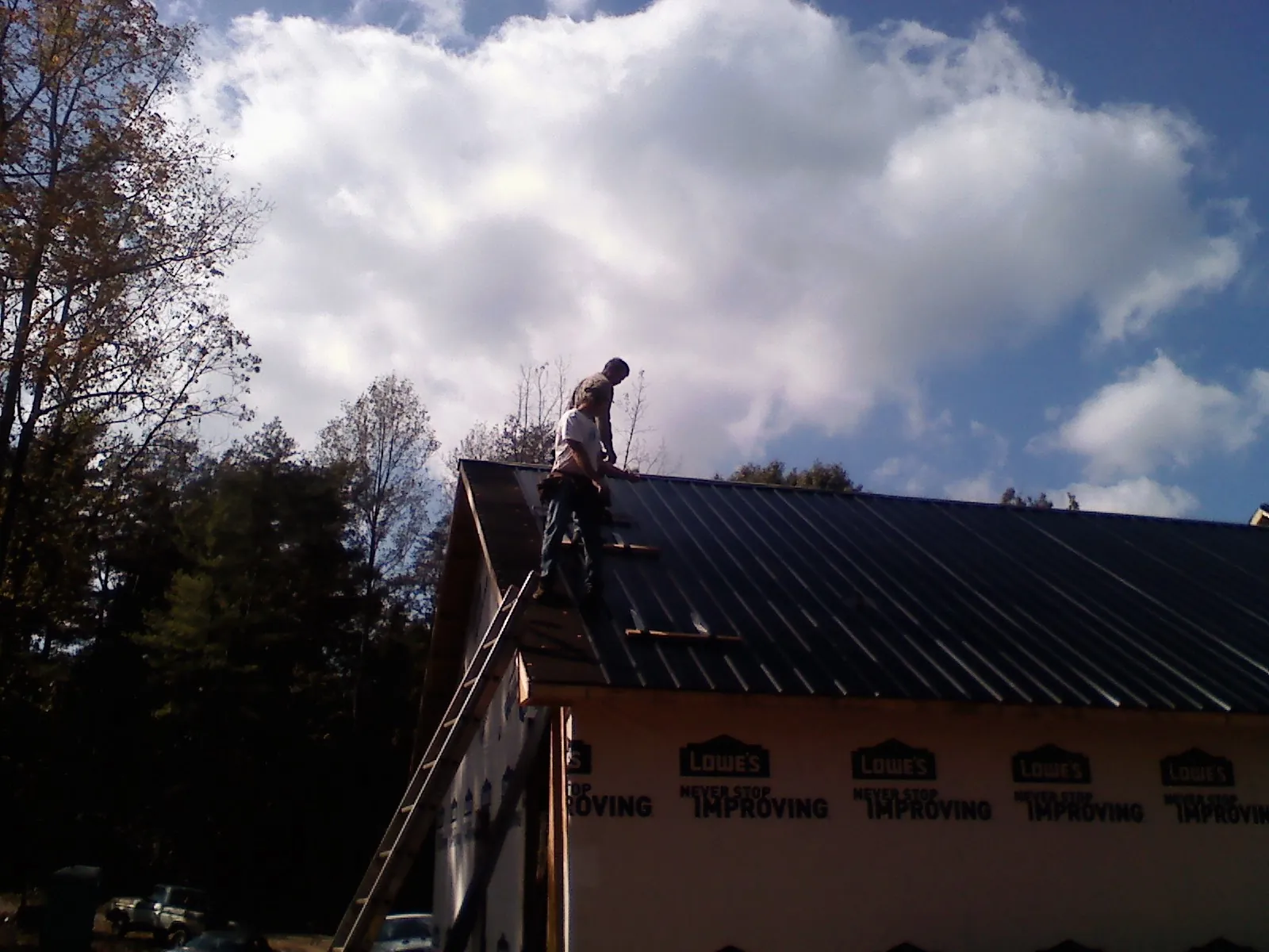 Roofer fastening dark metal panels high against a cloudy sky, from a Roof Inspection job in Wichita