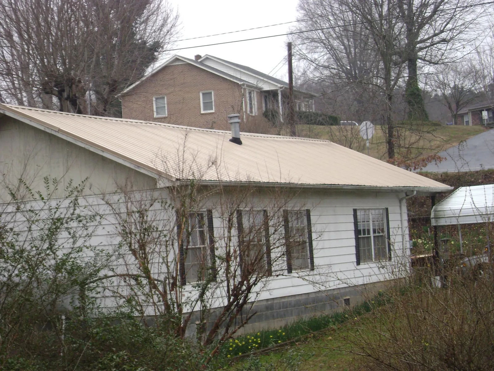Tan metal roof on a white sided house set into a hillside — Commercial Roofing by Roofing Brothers in Wichita